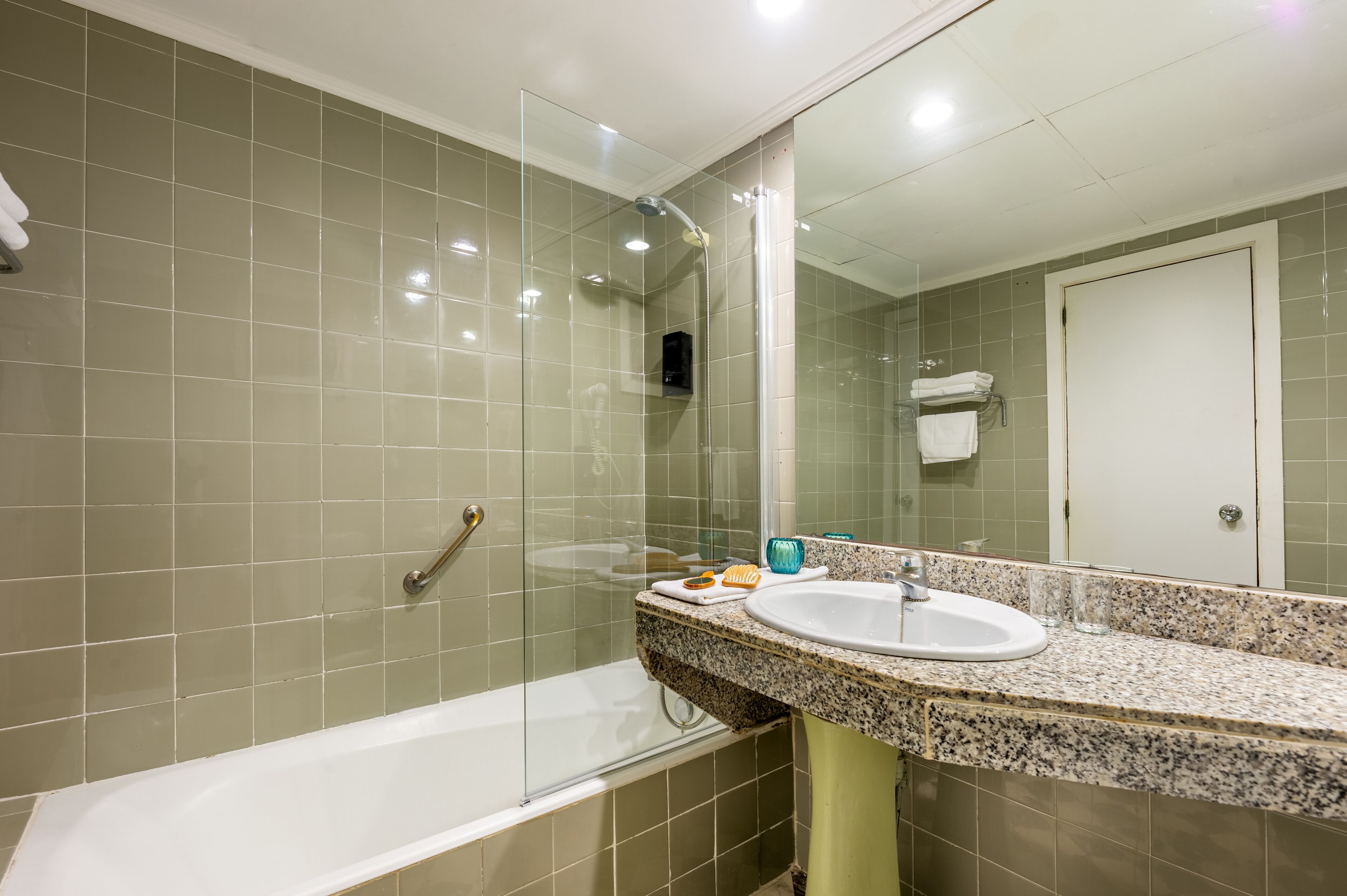 Een badkamer met een douchecabine van glas, een wastafel met een granieten aanrechtblad en een spiegel.