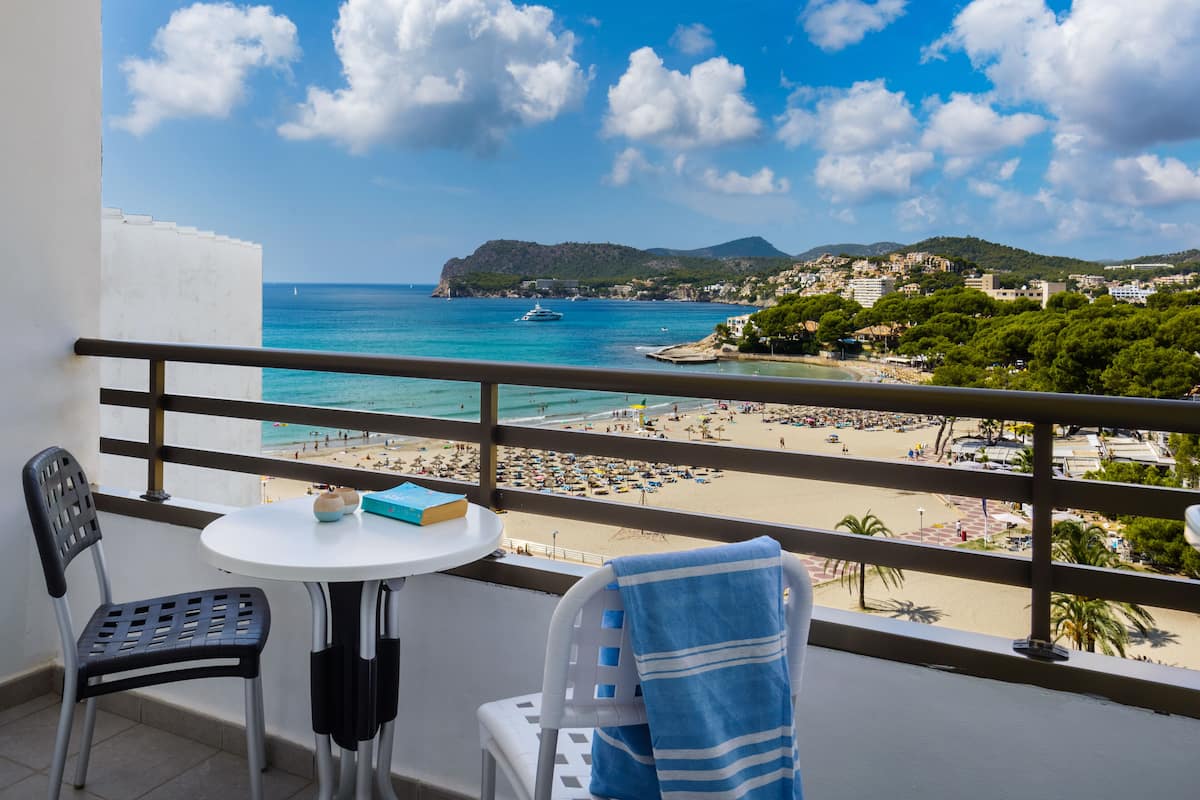 A balcony with a view of a beach, a table with a book, and two chairs.