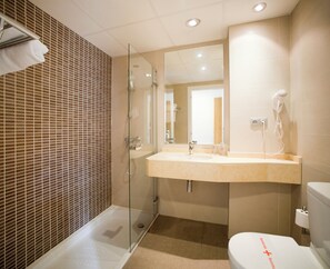 Un baño con cabina de ducha de vidrio, lavabo con espejo e inodoro.