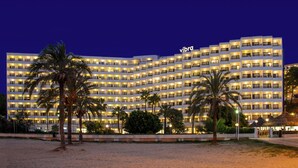 Un hotel grande de varios pisos con un llamativo letrero 'vibra', balcones y una fachada bien iluminada.