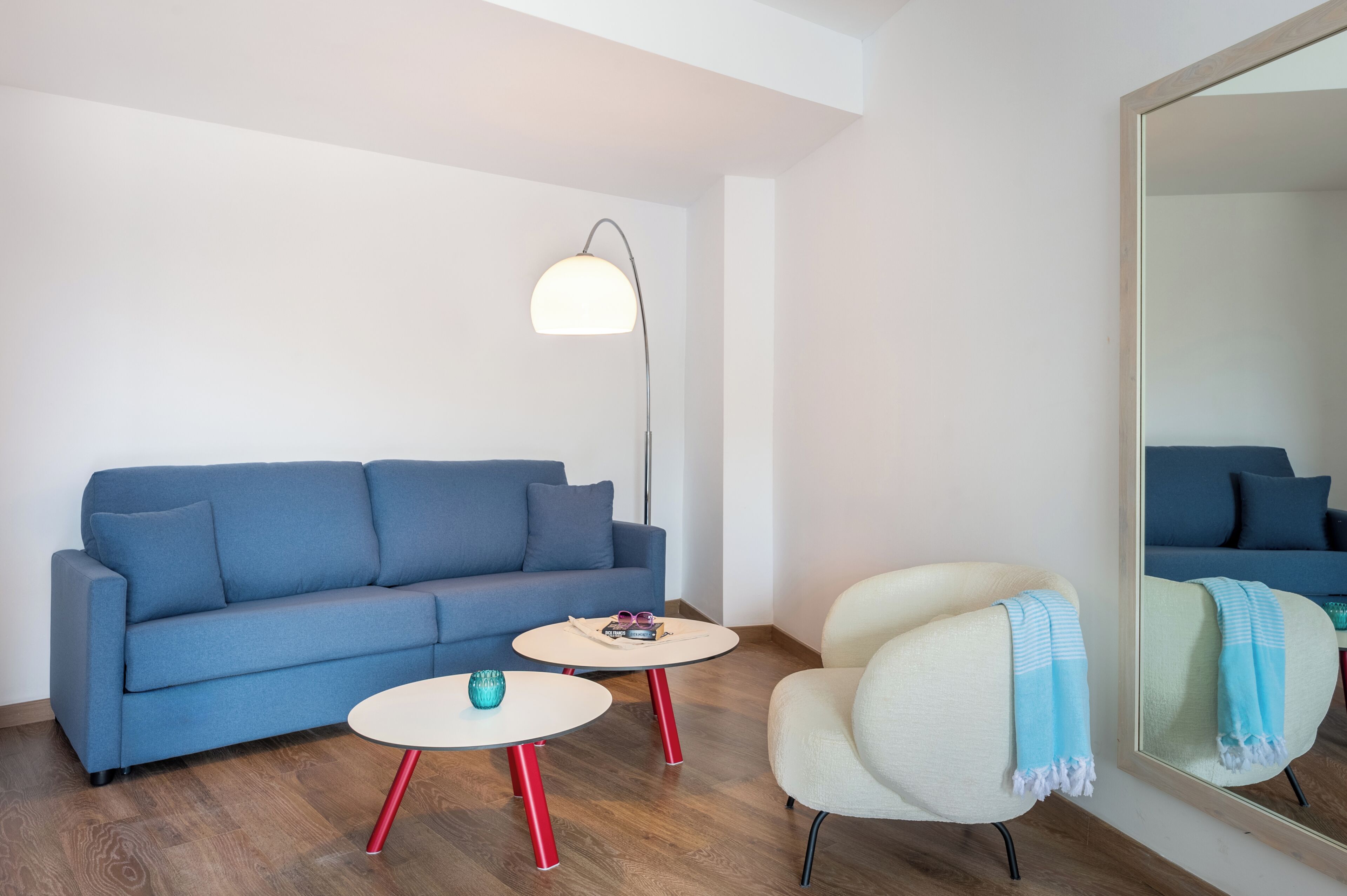 En moderne stue med en blå sofa, en hvid lænestol, et rundt sofabord og en gulvlampe.