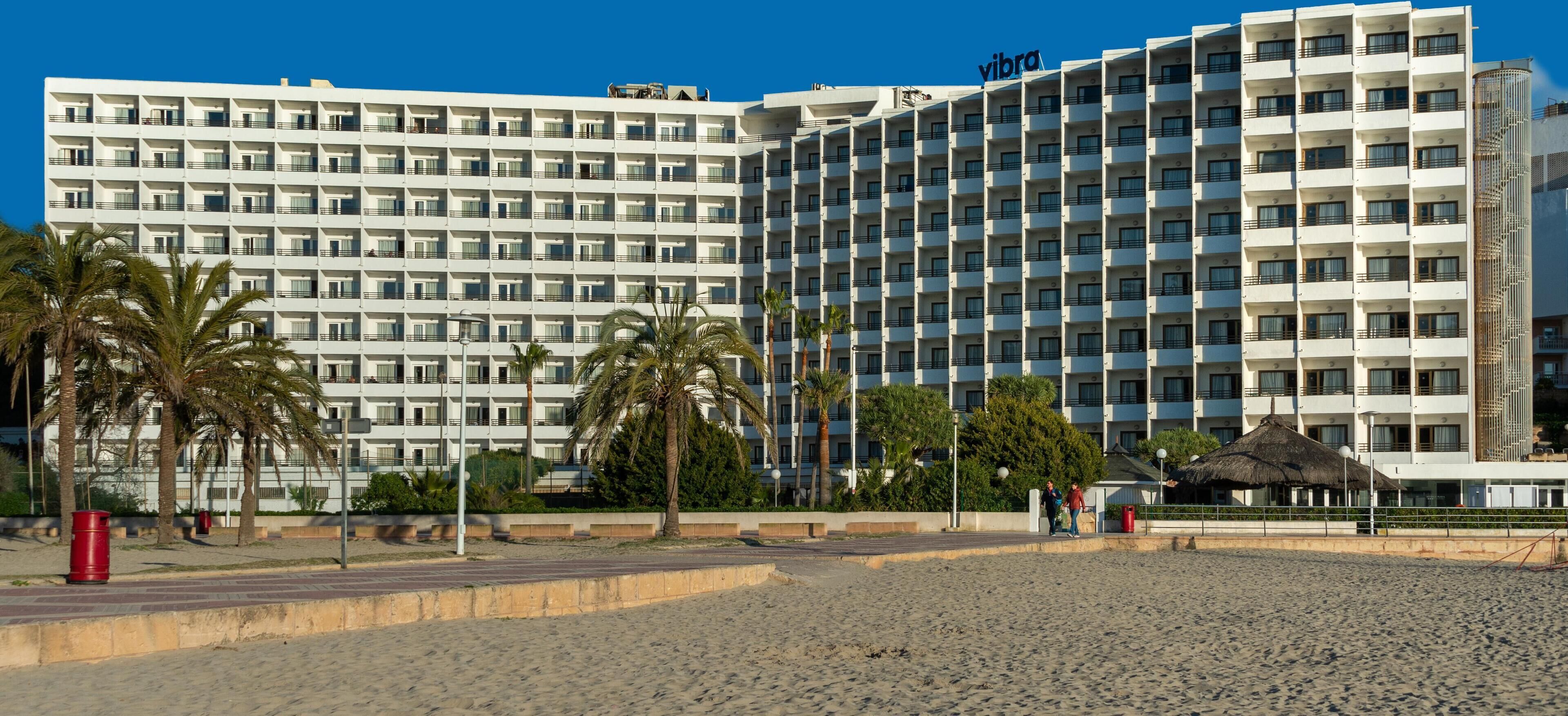 Un hotel moderno con varios pisos, balcones y ubicación frente a la playa.