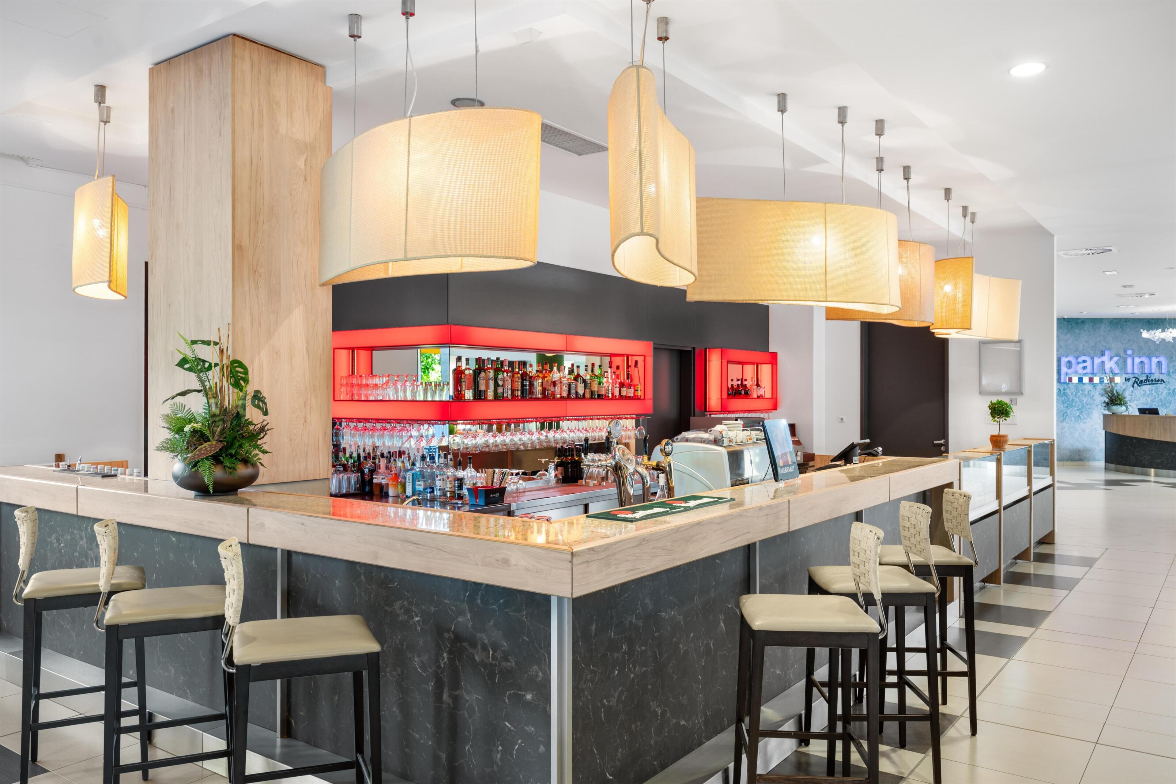 A modern bar area with a marble counter, multiple bar stools, hanging pendant lights, and a visible 'park inn' sign in the background.