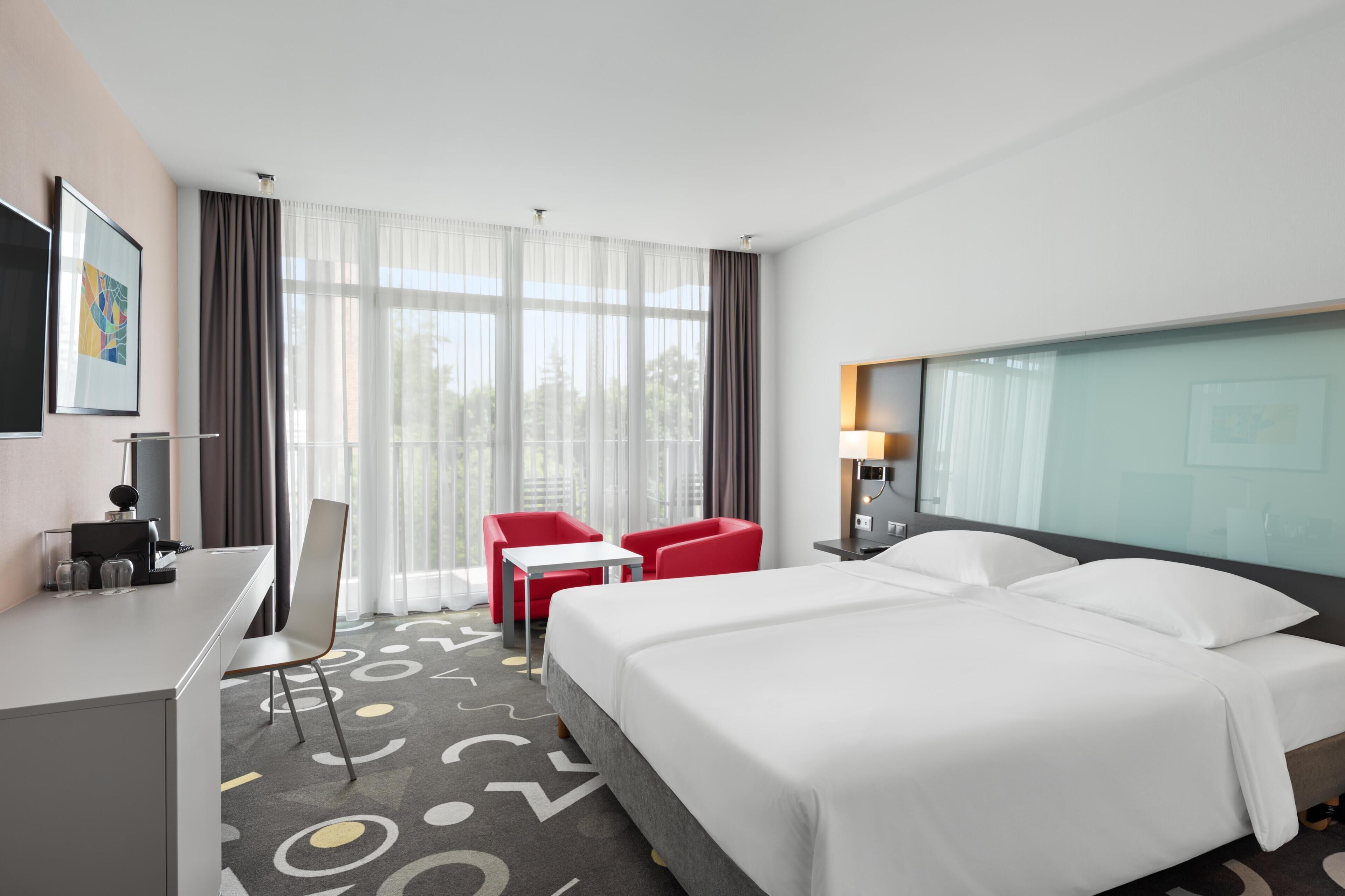 Une chambre d’hôtel avec un lit, un bureau, des chaises et une grande fenêtre.