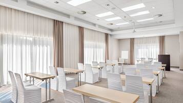 A conference room with rows of tables and chairs, large windows with curtains, and a podium.