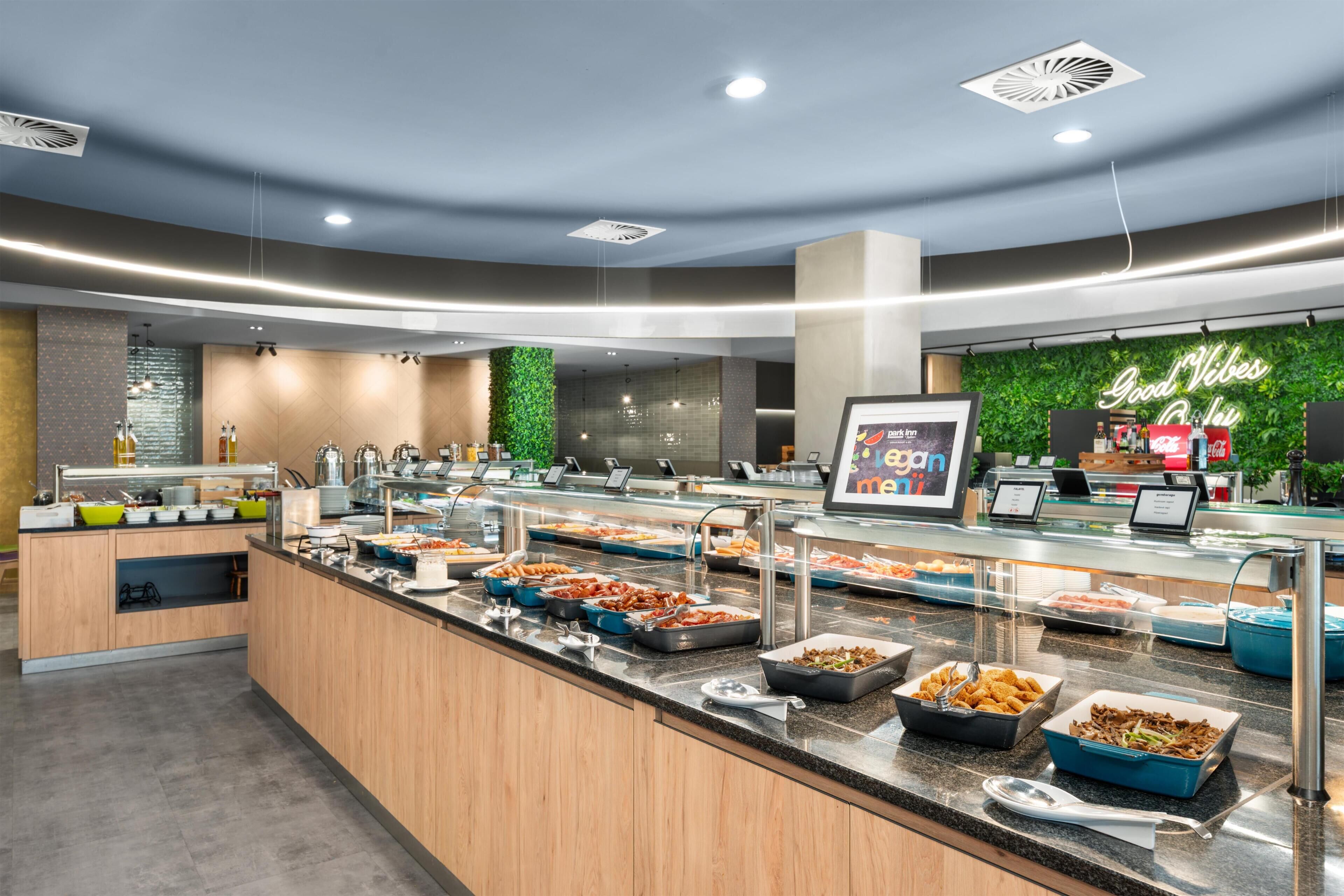 A buffet with various food options, a green wall with a 'Good Vibes' sign, and a modern kitchen area.