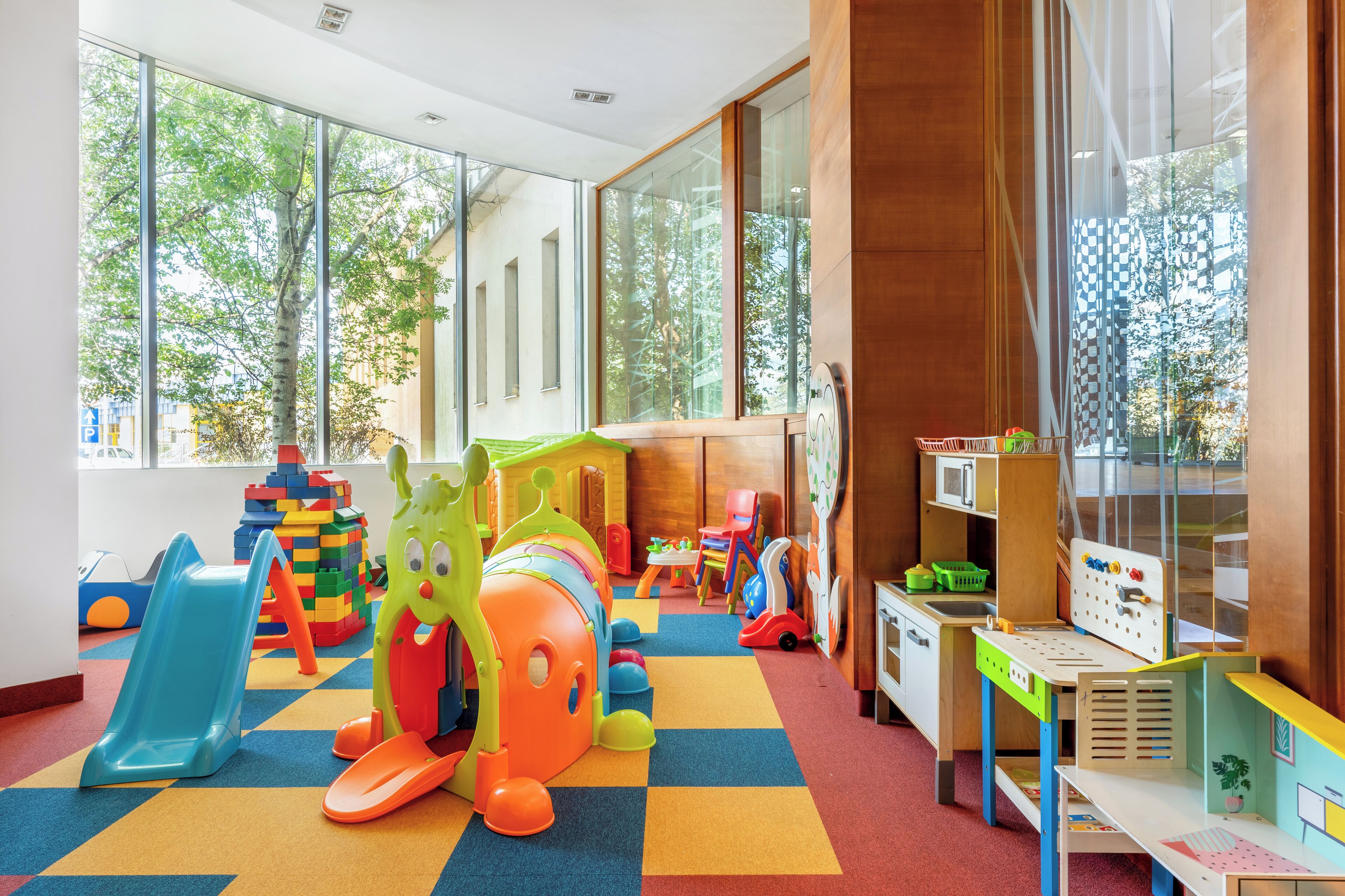 A children's playroom with colorful toys, a slide, and large windows.