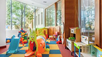 A children's playroom with colorful toys, a slide, and large windows.