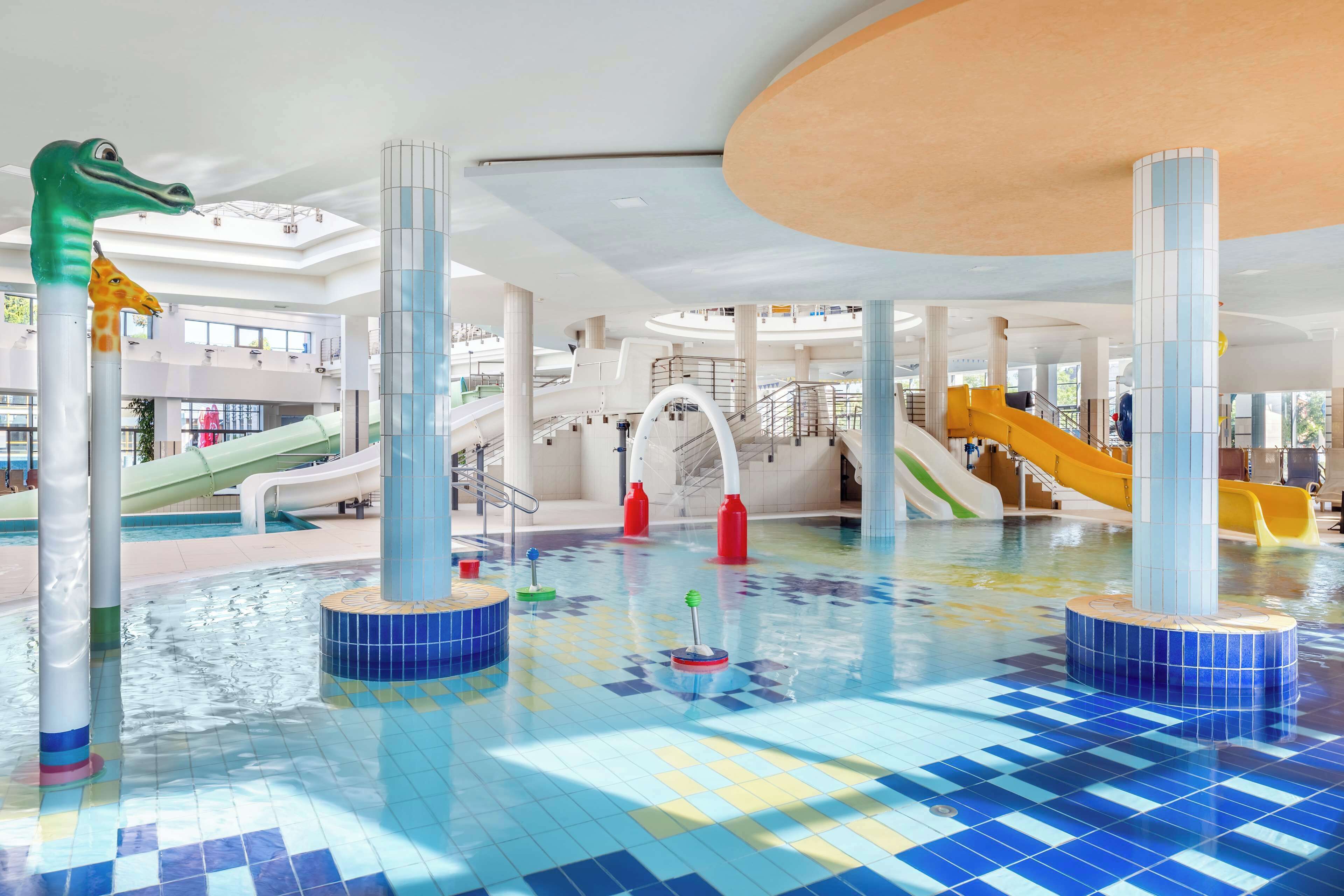 An indoor swimming pool with multiple slides and colorful tiled floors.