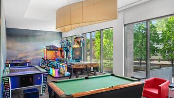 A pool table, arcade games, and a red chair in a room with large windows.