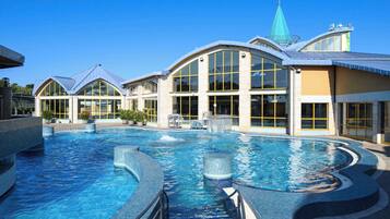 A large indoor swimming pool with a modern architectural design, surrounded by a building with large windows and a distinctive green spire.