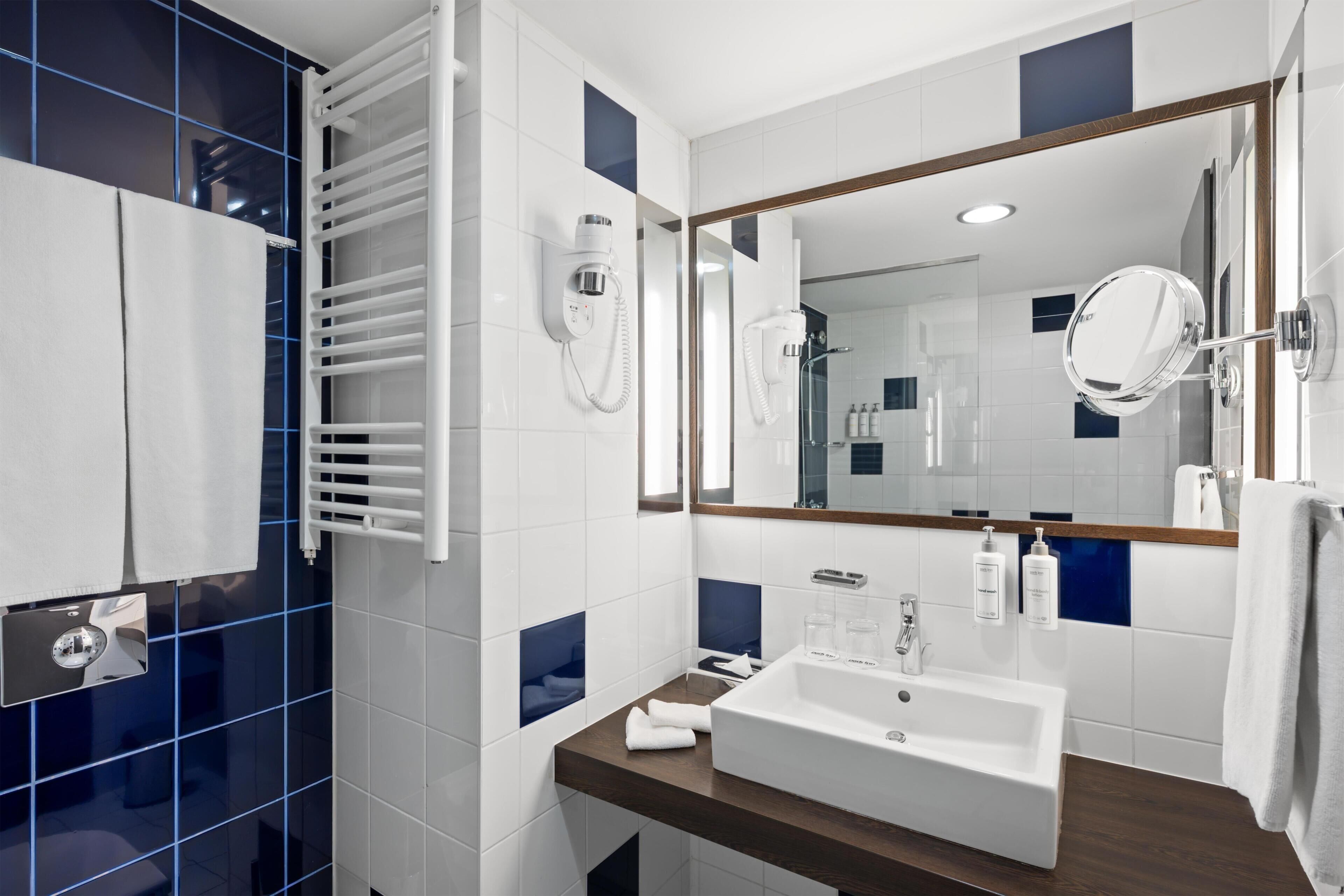 A modern bathroom with a large mirror, a white sink, and a towel rack.