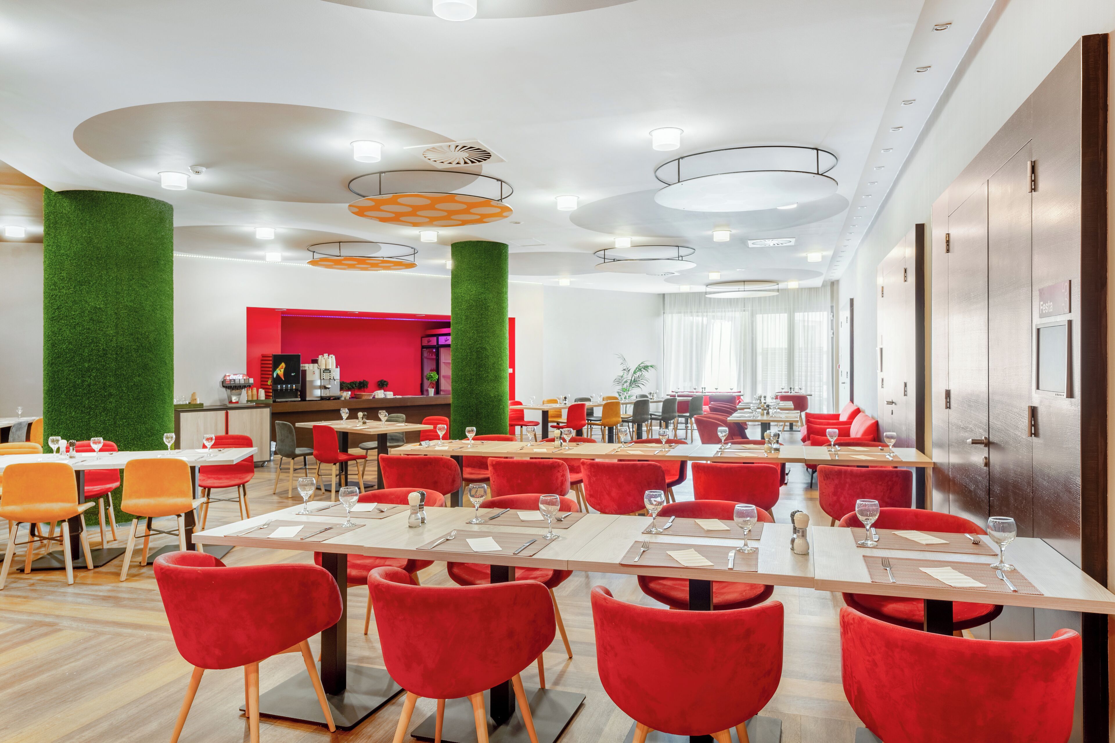 A modern dining area with red chairs, white tables, and a green accent wall.