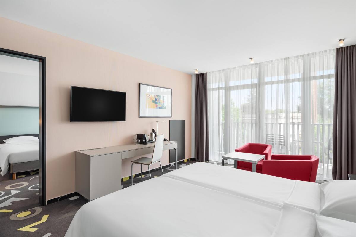 Hotellihuone, jossa on sänky, työpöytä, tuoli, televisio ja ikkuna, jossa on verhot.