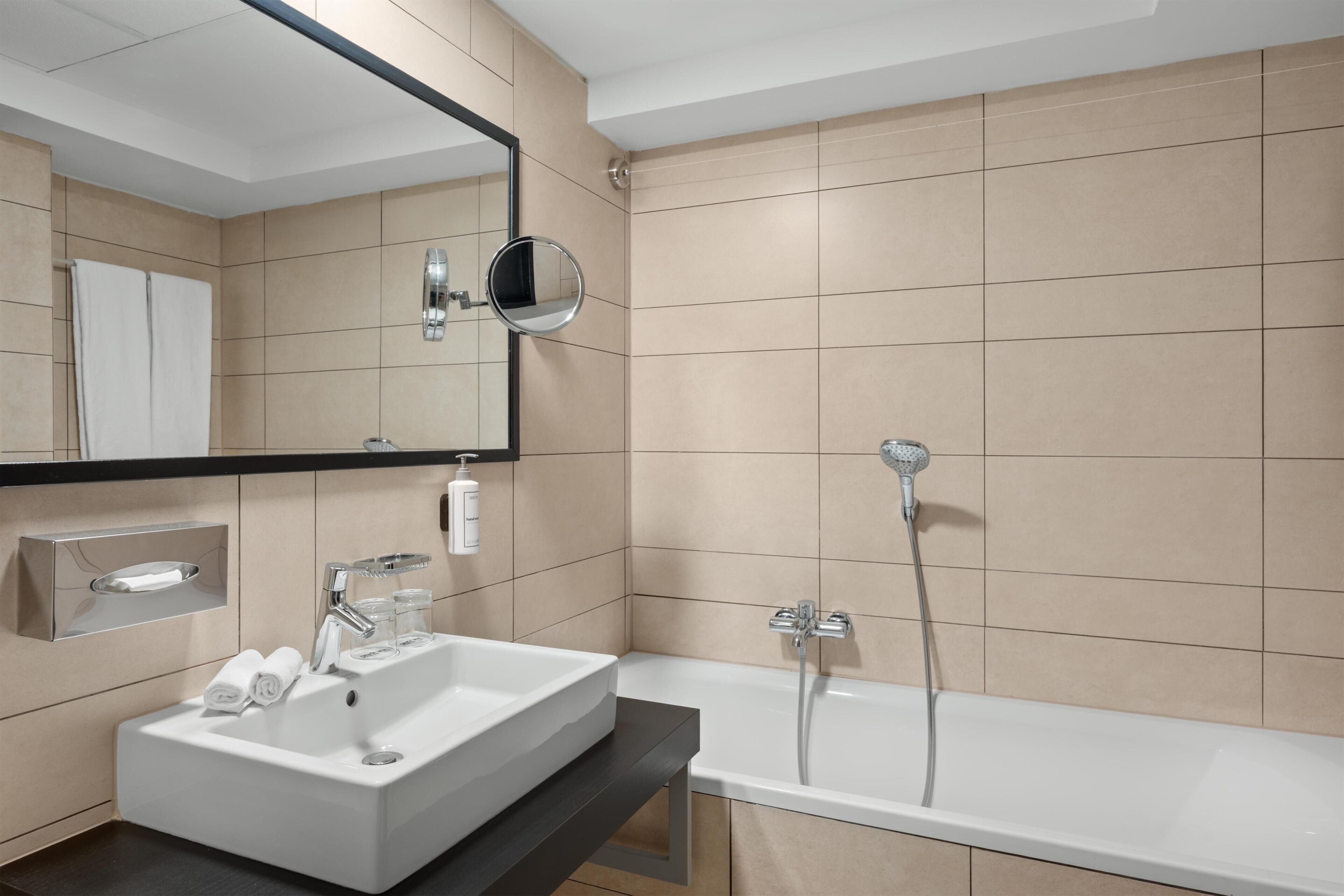 Un bagno moderno con un lavandino, uno specchio e una vasca da bagno bianchi.