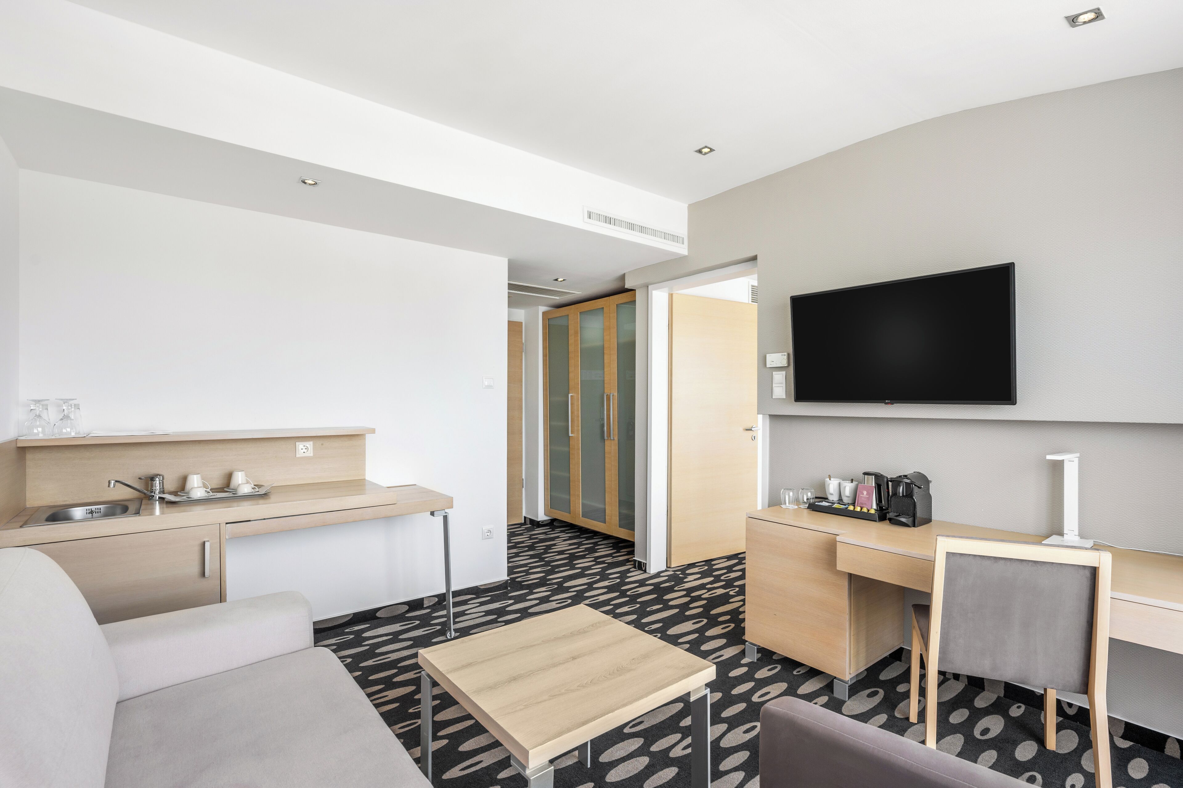 Une chambre d’hôtel moderne dotée d’une kitchenette, d’un téléviseur à écran plat, d’un canapé, d’une petite table et d’un tapis à motifs.