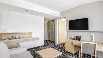 Une chambre d’hôtel moderne dotée d’une kitchenette, d’un téléviseur à écran plat, d’un canapé, d’une petite table et d’un tapis à motifs.
