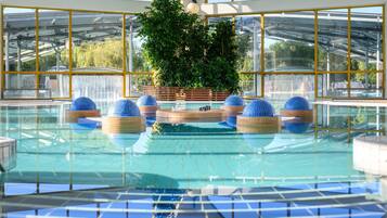 An indoor swimming pool with clear glass walls, blue spherical decorations, and a central plant area.