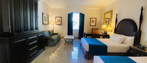 A hotel room with two beds, a desk, a sofa, a wardrobe, and a mirror.