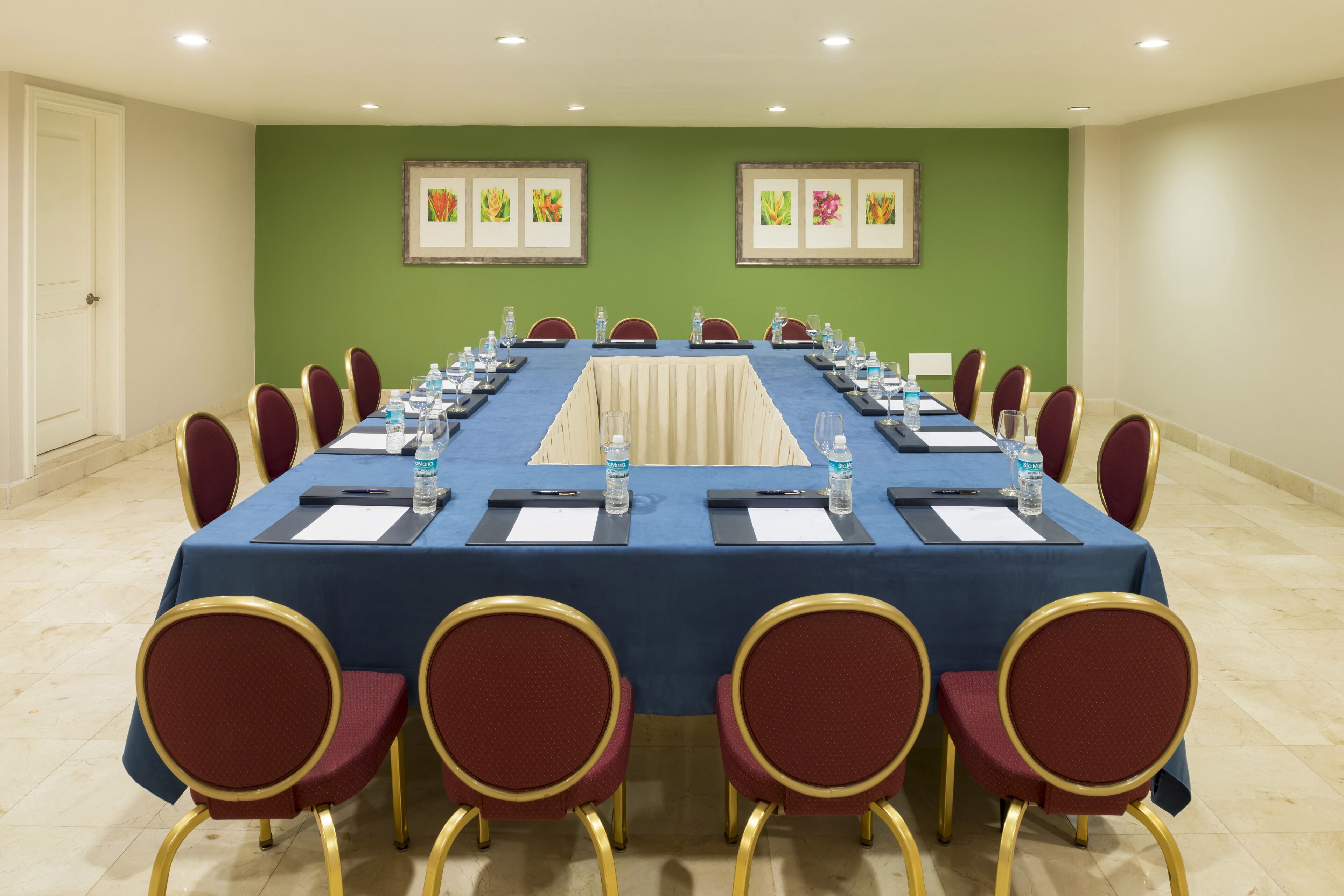Un salón de conferencias con una larga mesa, sillas rojas y botellas de agua.