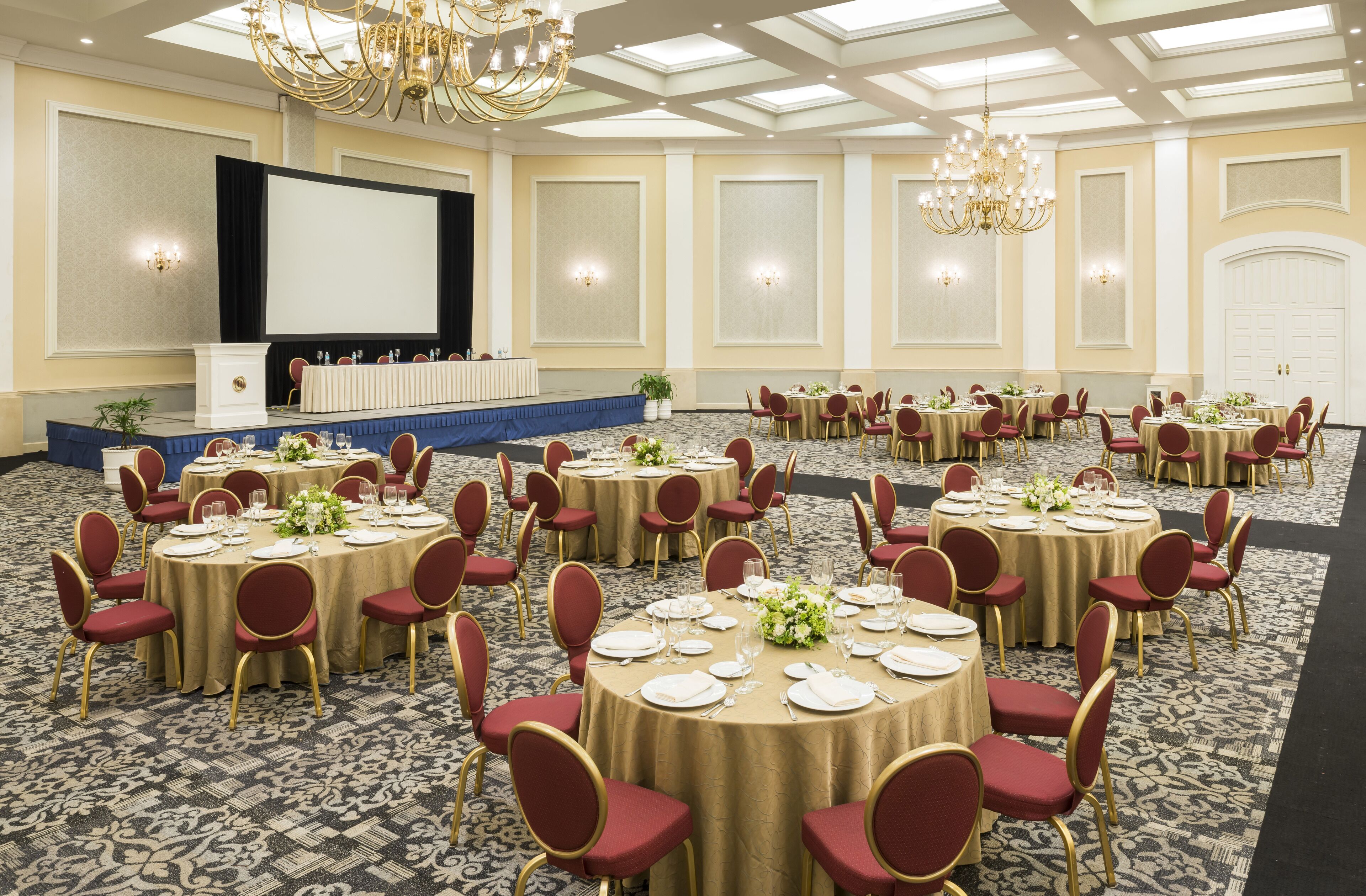 A banquet hall with round tables, red chairs, and gold accents.