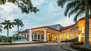 Un hotel con ingresso coperto, palme e un giardino curato.