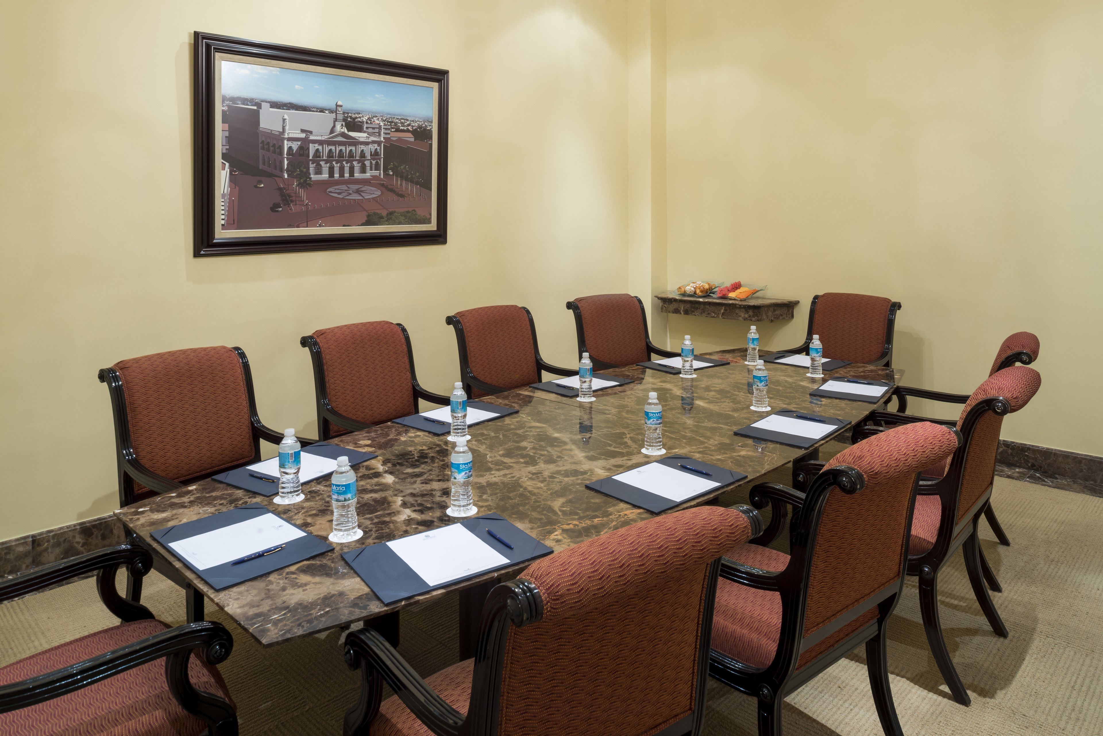 A conference room with a marble table, six chairs, water bottles, and a framed picture on the wall.