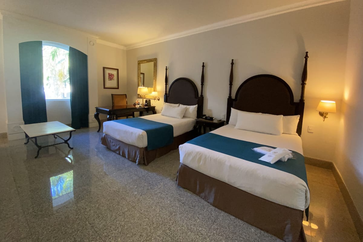Een hotelkamer met twee bedden, een bureau, een stoel, een spiegel en een raam.