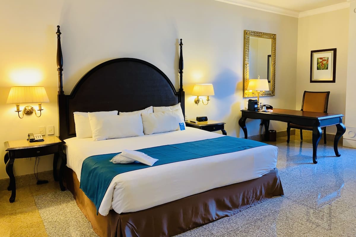 Een hotelkamer met een hemelbed, twee nachtkastjes, een bureau en een stoel.