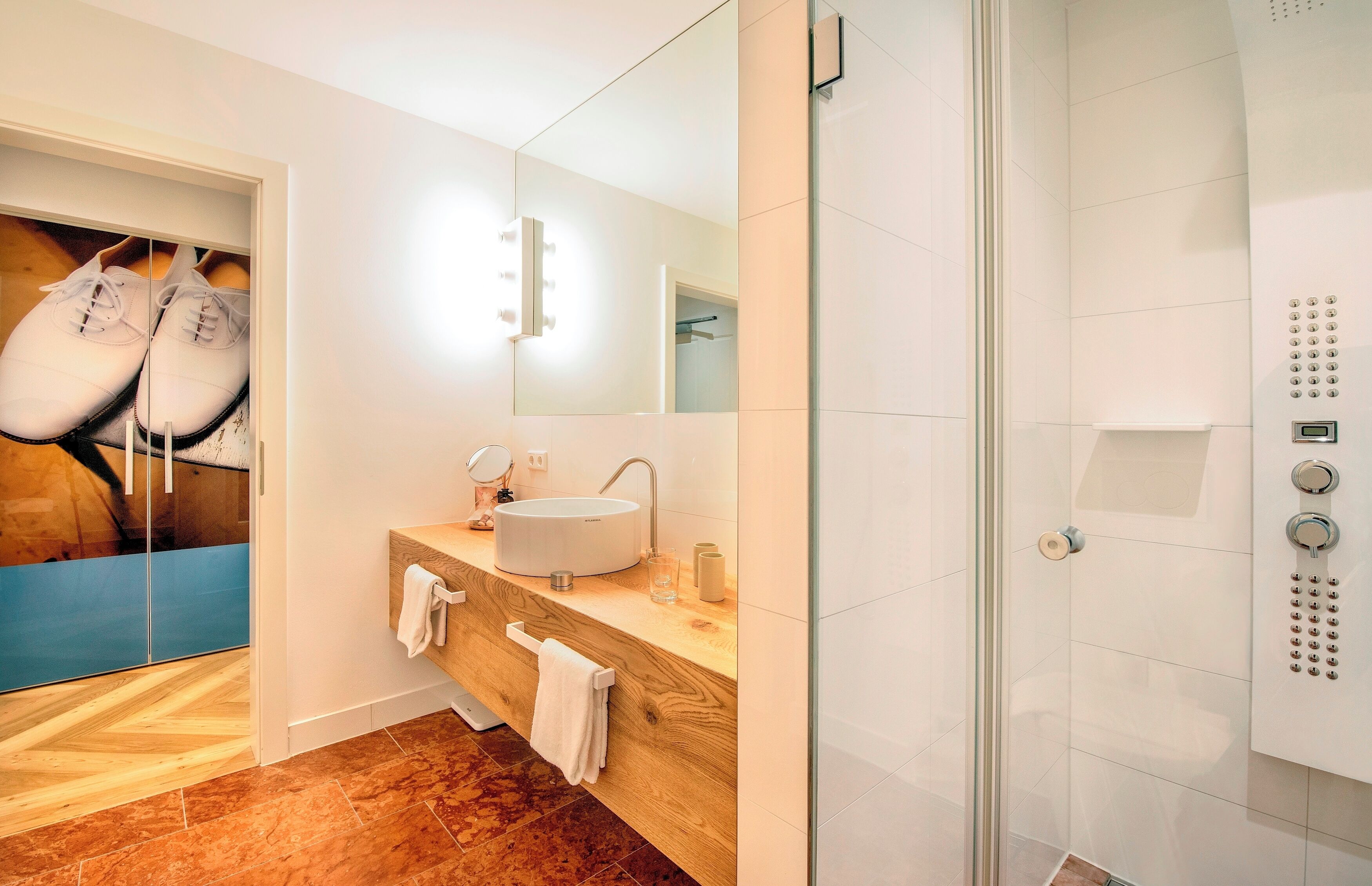 Un baño moderno con un espejo grande, un lavabo y una ducha con paneles de control.