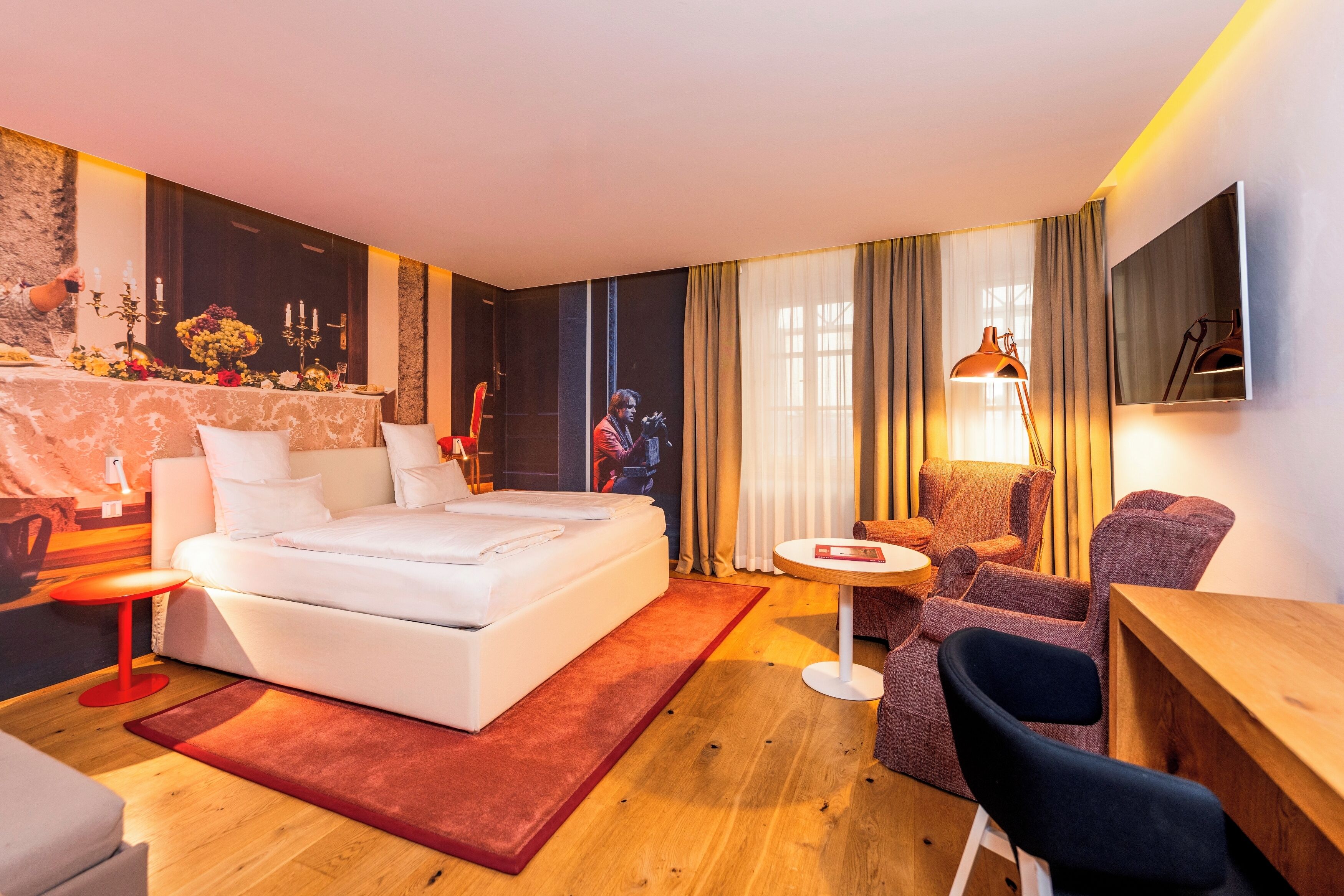 Una habitación de hotel moderna con una cama grande, una pequeña mesa redonda, un sofá y un televisor en la pared.