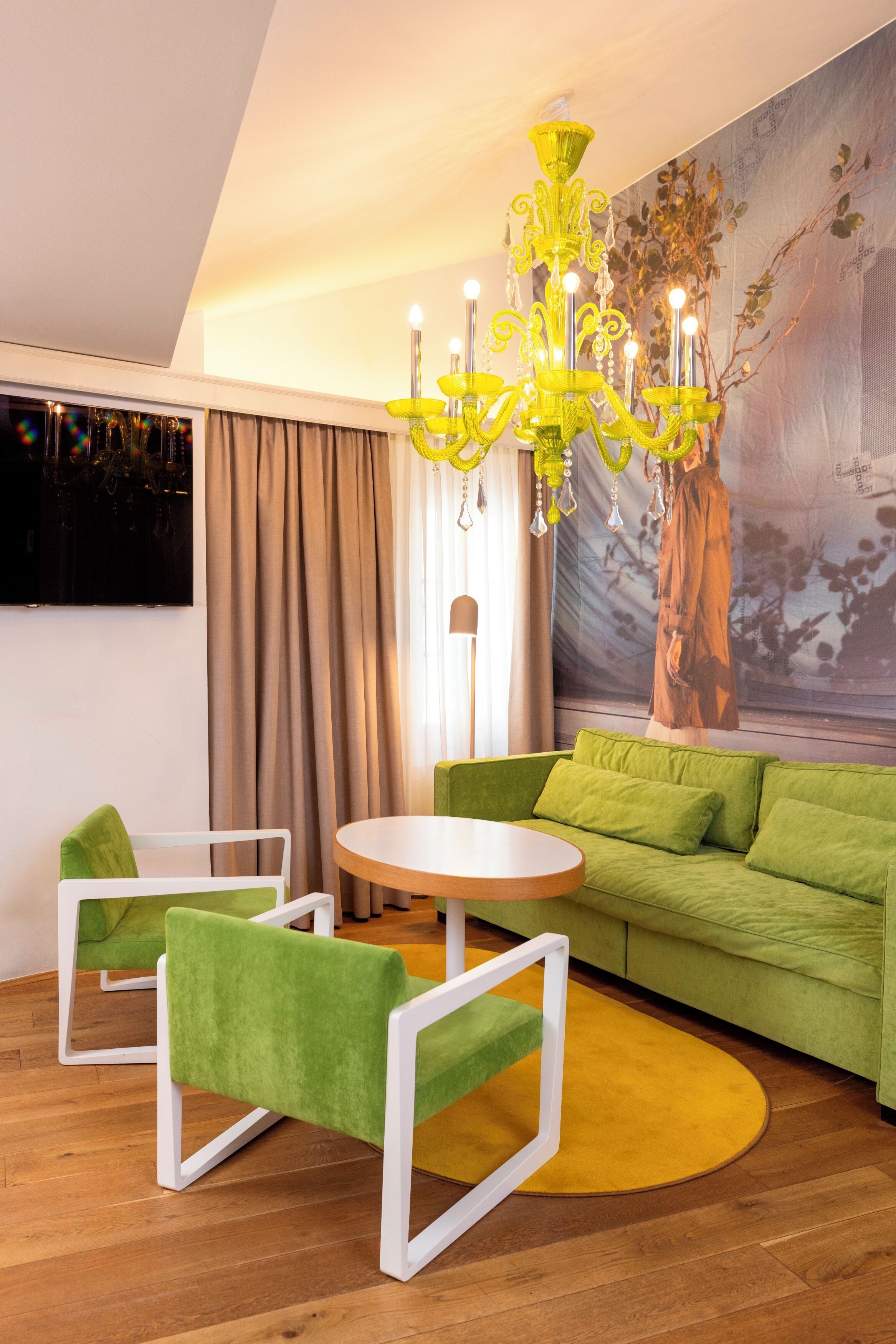 A modern living room with a green sofa, white armchairs, a round coffee table, and a yellow chandelier.