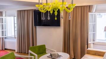 A modern living room with a round coffee table, green and beige sofas, a chandelier, and a flat-screen TV on the wall.