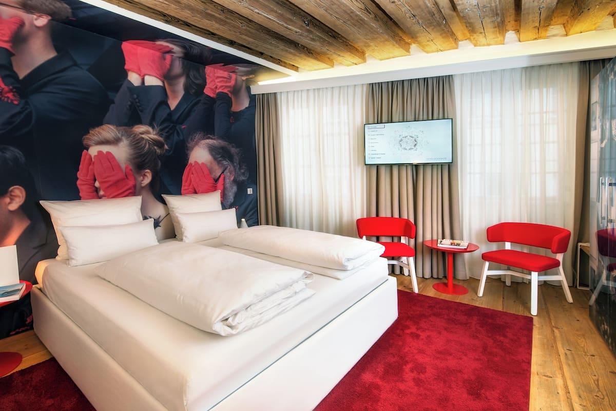 Ein Hotelzimmer mit einem großen Bett, zwei roten Sesseln, einem kleinen Tisch und einem Fernseher an der Wand.
