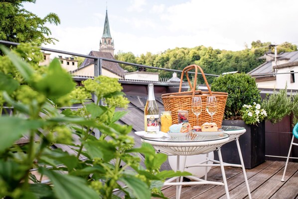 A balcony with a table set for a picnic, including a bottle, basket, and food items.