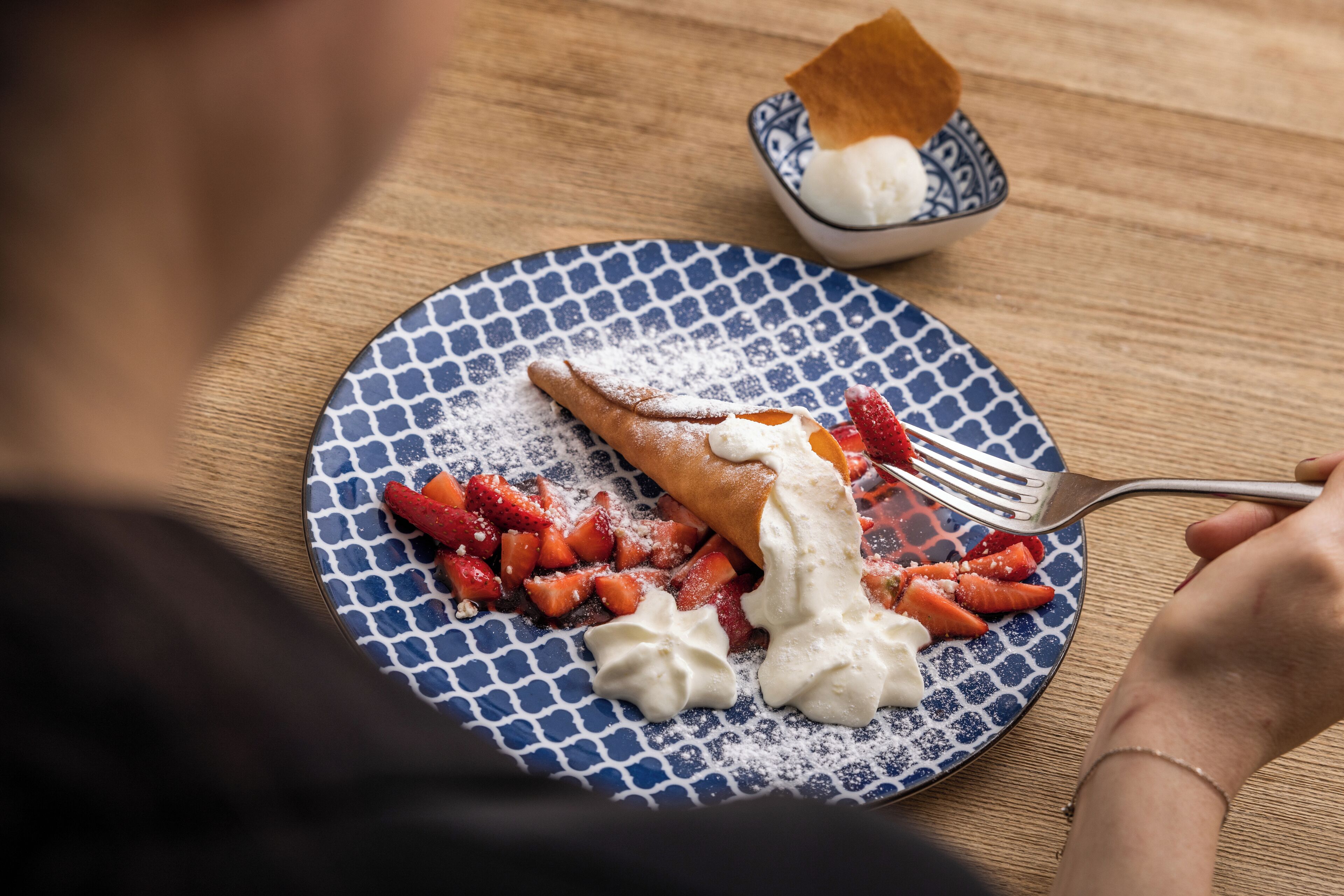 Un plato con un postre que incluye una crepa, fresas y crema batida.