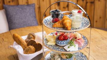 A three-tiered dessert stand with pastries, fruits, and cheese on a wooden table.
