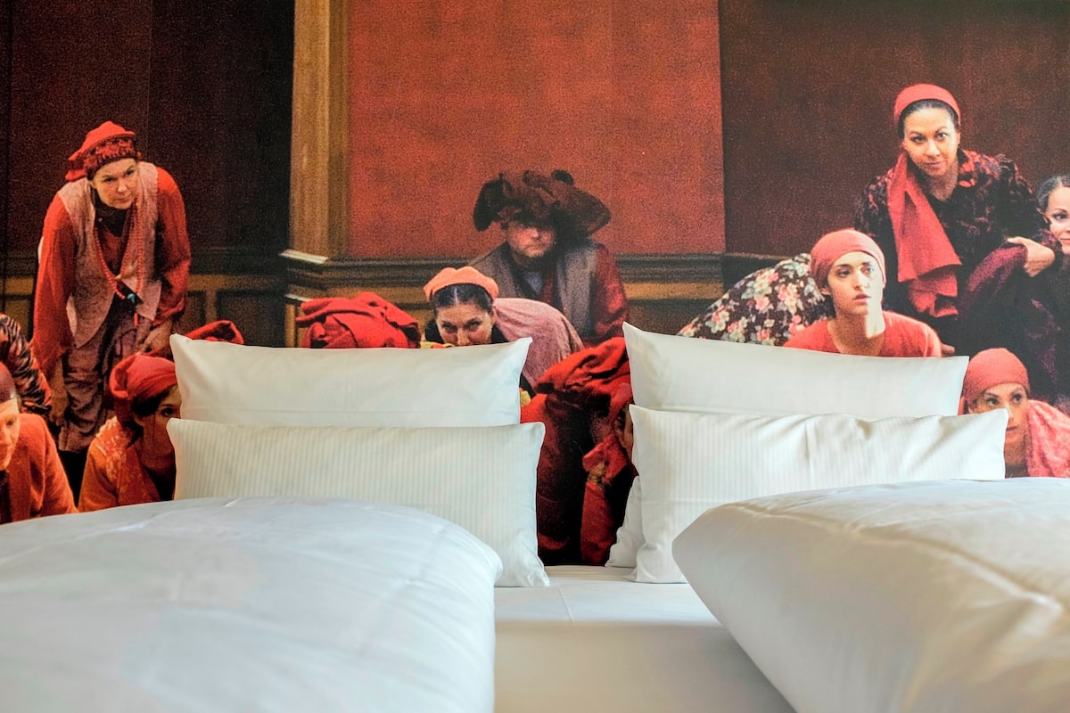 Ein Hotelzimmer mit einem Bett, Kissen und einer Personengruppe im Hintergrund.