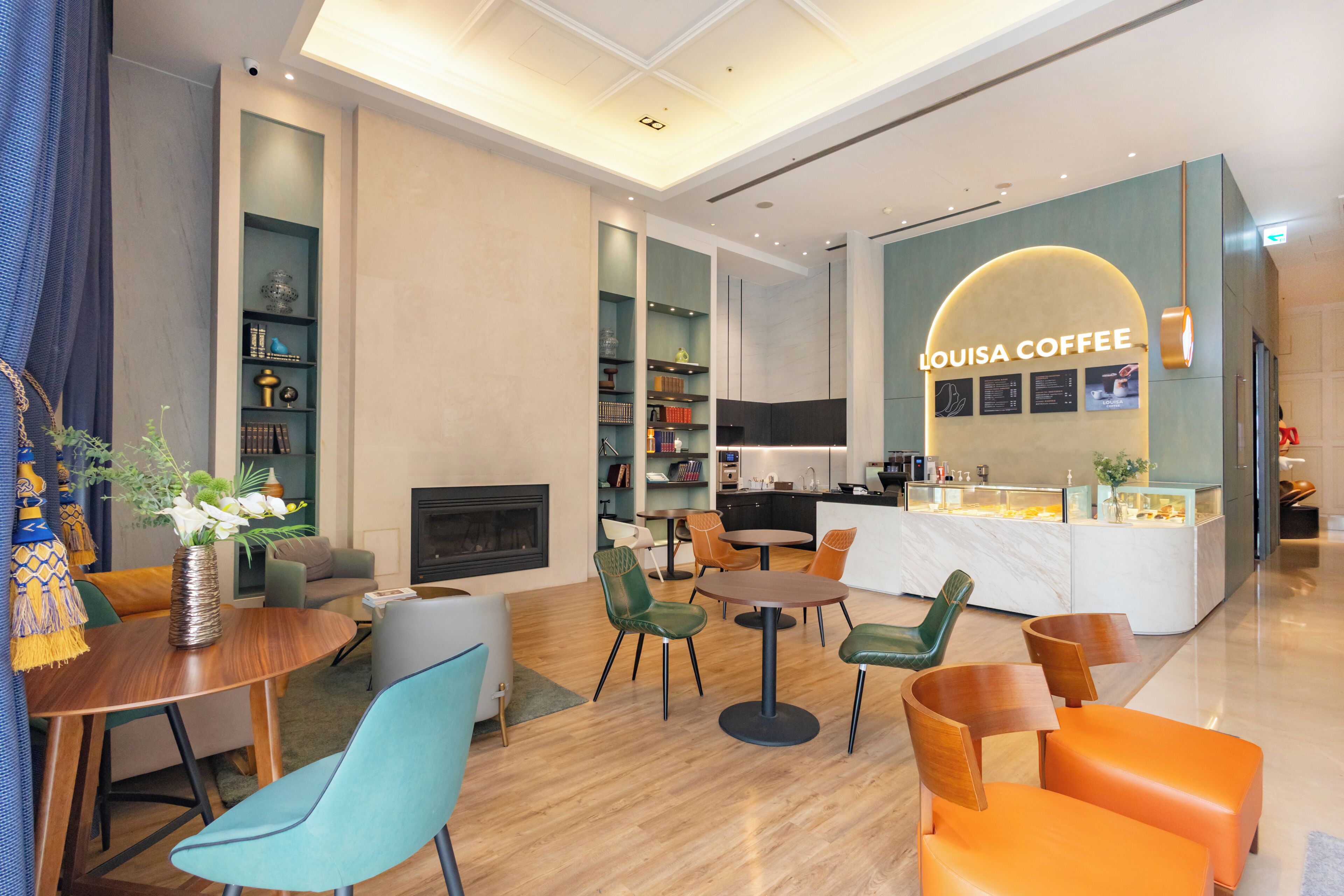 Un espace lounge moderne doté de sièges, d’une cheminée et d’un bar à café appelé « LOUISA COFFEE ».