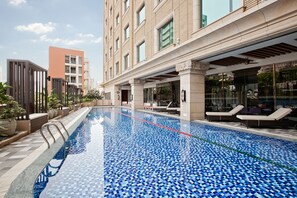 A swimming pool with a tiled floor, adjacent to a building with large windows and a covered entrance. - Miramar Garden Taipei (Taipei)