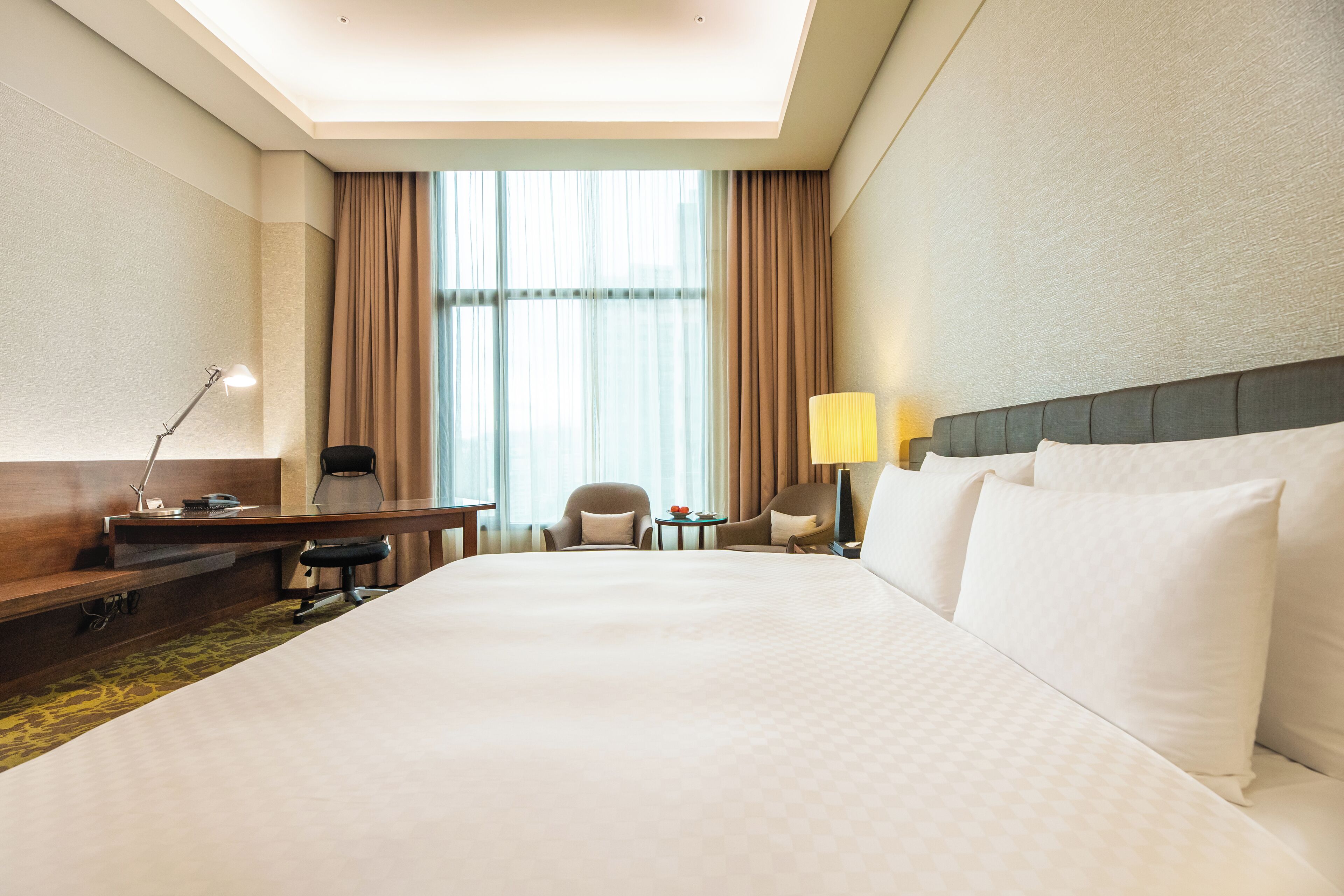 Habitación de hotel con una cama grande, un escritorio, dos sillas, una mesita y una lámpara.