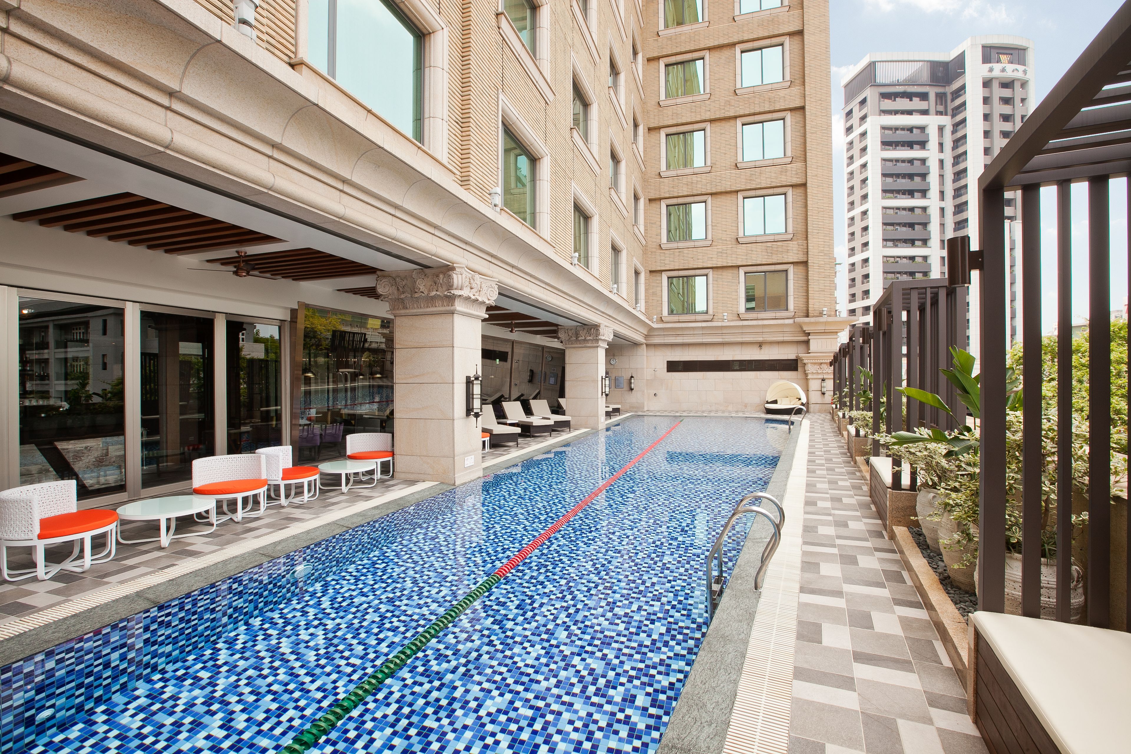 A swimming pool with lounge chairs and a covered seating area, surrounded by high-rise buildings.