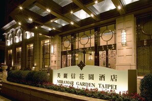 The exterior of Miramar Garden Taipei hotel with illuminated signage, large windows, and a well-maintained garden area. - Miramar Garden Taipei (Taipei)