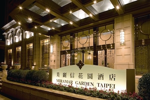 Het uiterlijk van hotel Miramar Garden Taipei, met verlichte borden, grote ramen en een verzorgde tuin.