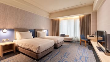 A hotel room with two beds, a desk with a TV, a chair, and a small table.