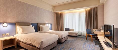 A hotel room with two beds, a desk with a TV, a chair, and a small table.