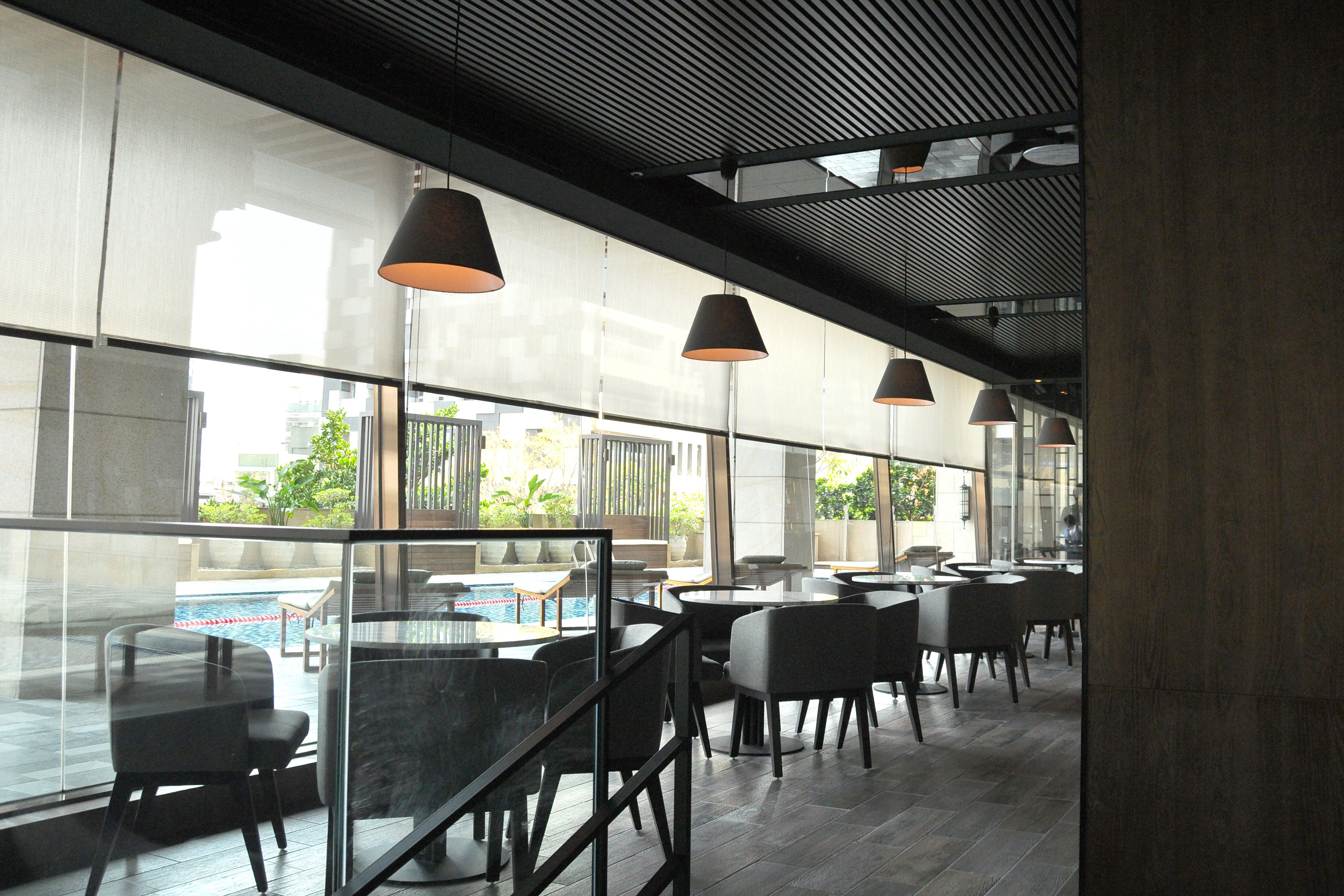 A modern indoor dining area with glass partitions, black chairs, and pendant lighting.