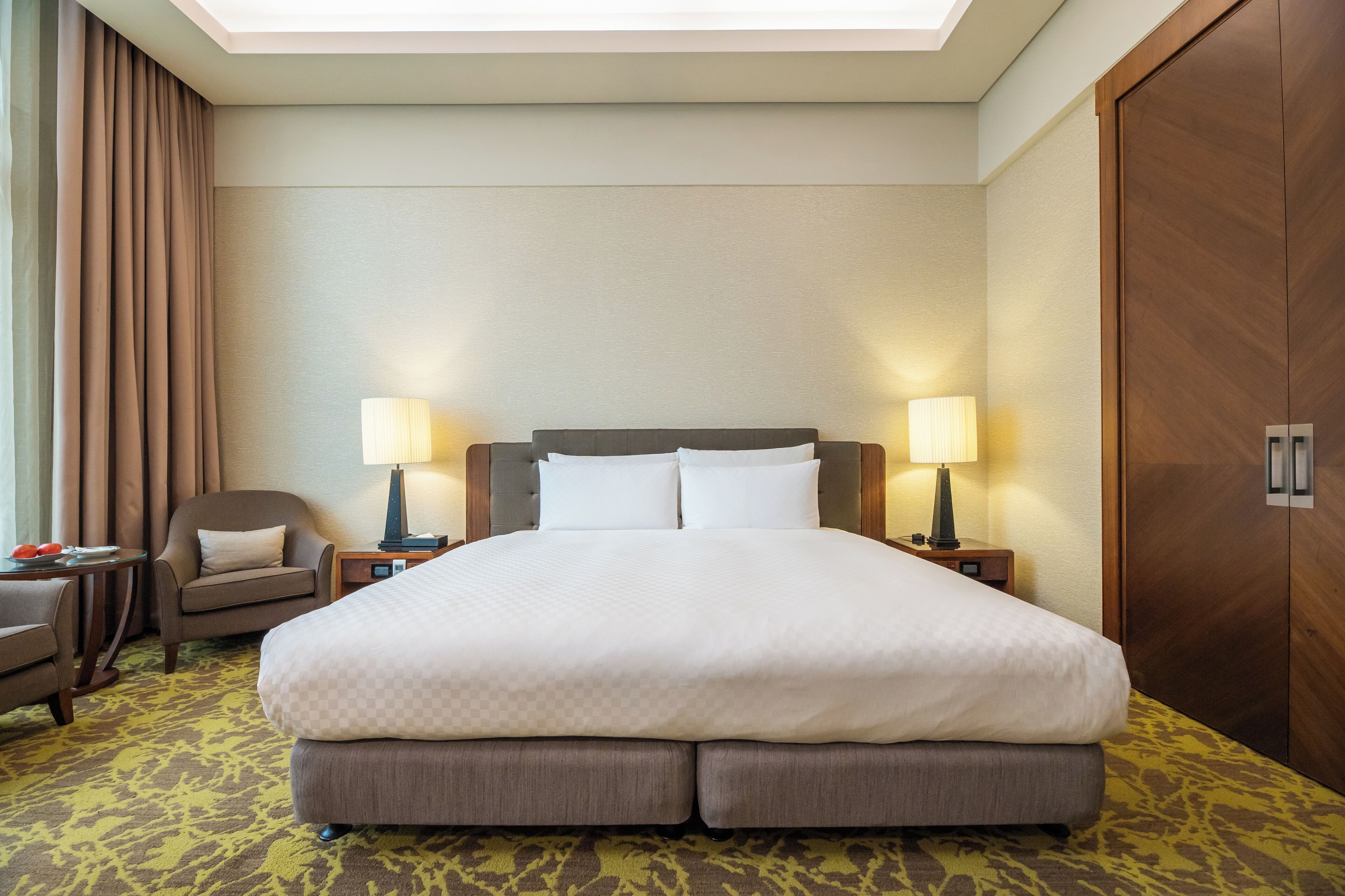 Een hotelkamer met een groot bed, twee nachtkastjes met lampen, een stoel en een kledingkast.