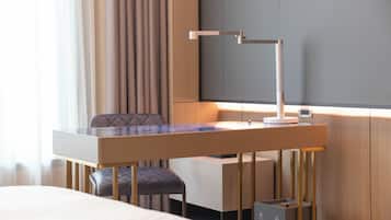 A hotel room with a bed, a desk with a lamp, a chair, and a wardrobe.