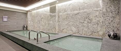A modern spa area with two rectangular pools, a wooden ceiling, and marble walls.